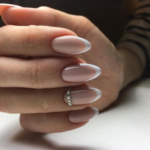 Français sur des ongles en forme d'amande. Dessins à la mode avec des strass, des étincelles, des trous, des frottements, des motifs délicats. Une photo