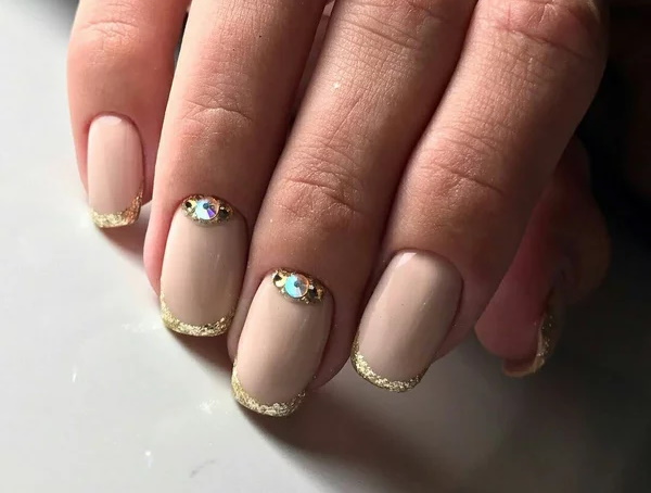 Manicure bege com brilhos, strass nas unhas curtas na base, fricção, estampa. Uma foto