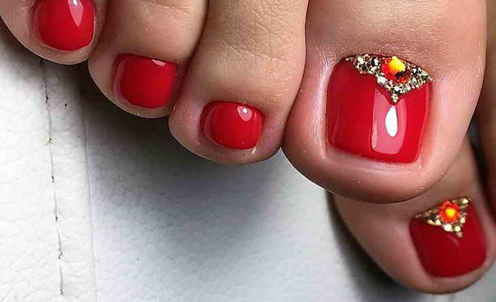 Pedicure vermelha nos pés. Foto com desenho, strass, padrões, esfregando