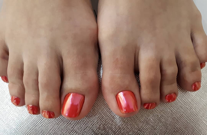 Pedicure vermelha nos pés. Foto com desenho, strass, padrões, esfregando